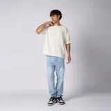 Remera oversize de lino entramado color blanco off-white, con cuello redondo, mangas cortas de hombro caído y etiqueta aplicada en el borde inferior.