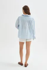 Camisa de algodón con detalles de broderie, volados y cuello a la base. Presenta diseño holgado, cierre frontal con botones y mangas largas con puños fruncidos.