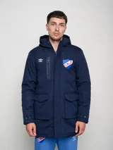 Parka larga de abrigo color azul marino, con capucha, cierre frontal, bolsillos con solapa y bolsillo superior con cierre. Presenta el logo de Umbro y el escudo del Club Nacional de Football.