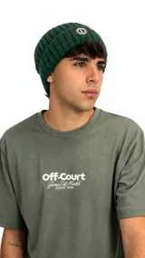 Gorro tipo beanie de punto acanalado en color verde oscuro, con parche circular con logo en la parte frontal.