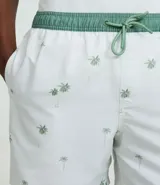 Bermuda de baño para hombre confeccionada en microfibra ligera, color blanco, con una estampa sutil de cocoteros en tonos verdes/azulados. Presenta cintura elástica con cordón de ajuste contrastante en color verde, y bolsillos laterales.