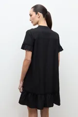 Vestido corto negro de corte amplio, con cuello mao, mangas cortas con volados y detalles de vainillas verticales en el frente. Cuenta con un volante fruncido en el ruedo.