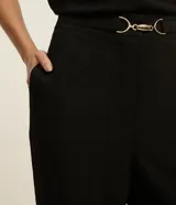 Pantalón negro de corte zanahoria, con cintura elástica, adorno metalizado en la cintura y bolsillos laterales.