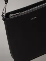 Cartera tipo saco pequeña Calvin Klein color negro, de cuero sintético granulado. Tiene dos correas desmontables: una correa fina ajustable y una correa ancha ajustable con logo jacquard.
