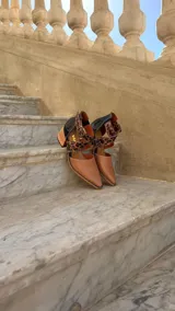 Zapatos de cuero color tostado con puntera fina y taco bloque de madera de 6 cm. Cuentan con tiras cruzadas con estampado animal print de leopardo en el empeine, talón negro y tira al tobillo con hebilla metálica ajustable.