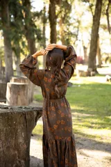 Vestido largo de lino con escote en V, mangas largas abullonadas y falda con volado en el ruedo. Presenta un estampado floral en tonos tierra sobre base marrón.