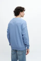 Buzo celeste de corte holgado con cuello redondo y puños y cintura acanalados. Estampado frontal con texto "Sunset Whispers" en color azul.