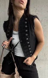 Chaleco negro de denim estilo militar, con doble botonadura metálica frontal, cuello alto y detalles deshilachados en las sisas.