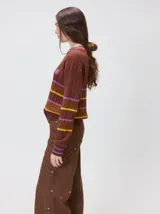 Sweater clásico de punto cable con cuello redondo a la base, mangas largas y fit al cuerpo. De color marrón con franjas horizontales violetas y amarillas, cuenta con el cuello, puños y ruedo acanalados, además de un pequeño logo bordado en el pecho.
