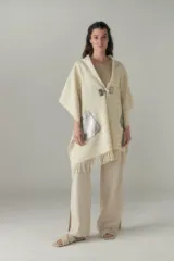 Chal de lana fina sin teñir con diseño de cuadros sutiles, cierre frontal con alamar y bolsillos de cuero metalizado. Presenta terminaciones con flecos en el ruedo y un calce estructurado en los hombros.