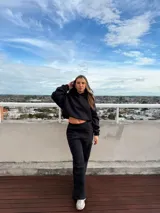 Conjunto deportivo compuesto por un buzo corto con capucha y un pantalón de corte wide leg, ambos en color negro. El buzo presenta un diseño holgado y el pantalón cuenta con cintura elástica.