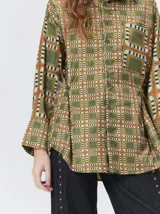 Camisa de seda con cuello camisero, manga larga y bolsillo frontal. Presenta un diseño estampado geométrico de cuadrados en tonos marrones y azul oscuro.