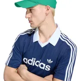 Remera deportiva Adidas Originals azul marino de manga corta, con cuello polo y solapa en V de color blanco. Presenta las icónicas tres tiras blancas en los hombros, el logotipo clásico de la marca en el pecho y un sutil patrón de rayas verticales tejidas.