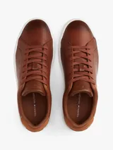Zapatillas de estilo tenis Tommy Hilfiger confeccionadas en piel color marrón, con diseño de corte bajo, cordones al tono y suela de goma blanca. Presenta un panel de gamuza a contraste en el talón y el logo de la marca grabado en el lateral.