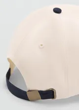 Gorra Archive de color beige con visera y botón superior azul marino. Cuenta con mensaje bordado en el lateral y cierre regulable con hebilla metálica.