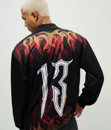 Remera de manga larga con corte boxy, confeccionada en microfibra de poliéster. Presenta un diseño estampado con motivos de llamas en tonos rojos y naranjas, junto con el número 13 en tipografía gótica en la espalda.