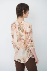 Camisa de manga larga con fondo verde y estampado floral en tonos rosados y beige, cuello redondo con pequeña abertura en V y cierre frontal con botones.