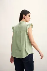 Camisa color amarillo pálido con textura arrugada, cuello mao con volados, cierre frontal con botones y mangas cortas con volados.