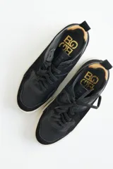 Zapatillas negras de cuero y gamuza, con cordones y suela blanca.