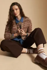 Cardigan corto de tejido jacquard con diseño geométrico en tonos beige y crema, con cierre frontal de botones y cuello redondo.