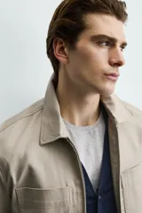 Sobrecamisa negra de corte relajado, confeccionada en tejido con mezcla de algodón elástico. Presenta cuello solapa, cierre frontal de cremallera, bolsillos de plastrón en el pecho y bolsillos de vivo en la cadera.