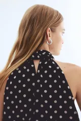 Top de corte holgado en tejido transparente con escote halter y cuello alto estilo pañuelo con cierre de botón en la nuca. Presenta un diseño con estampado de lunares y forro interior.