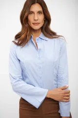 Camisa de manga larga, color celeste claro, con finas rayas verticales blancas. Presenta cuello camisero y calce entallado.