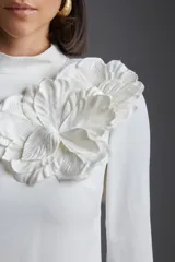 Vestido corto blanco de corte recto, con cuello alto, mangas 3/4 y aplique floral en el hombro.