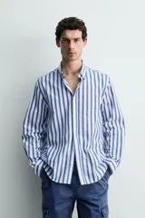 Camisa de corte regular fit confeccionada en tejido de algodón, con diseño de rayas verticales en azul y blanco. Presenta cuello solapa con botones, cierre frontal de botones, manga larga con puños abotonados y un bolsillo en el pecho.