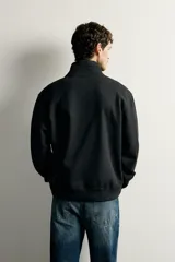 Sudadera negra de corte regular fit, con cuello subido, cierre frontal de cremallera corta y acabados en rib elástico en puños y cintura.