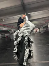 Conjunto de saco y pantalón plateado con estampado de flores negras. El saco es de corte deportivo con cierre y volados en el cuello y mangas. El pantalón es de corte ancho.