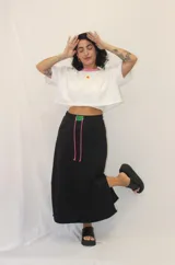 Falda larga de estilo deportivo confeccionada en tejido de algodón y poliéster. Presenta cintura elástica con cordón de ajuste en color fucsia, bolsillos laterales y un aplique decorativo de acrílico en la parte frontal.