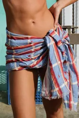 Pareo rectangular con estampado a cuadros en tonos celeste, naranja y blanco, con detalle de flecos en los bordes.