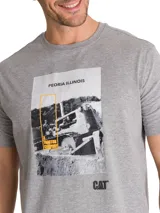 Remera gris melange de manga corta y cuello redondo, con estampa frontal fotográfica en blanco y negro con detalles en amarillo y la inscripción "PEORIA ILLINOIS" junto al logo de CAT.