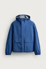 Cazadora técnica relaxed fit de color azul, con cuello subido, capucha ajustable, bolsillos frontales de plastrón con solapa, cierre de cremallera oculta y puños elásticos.