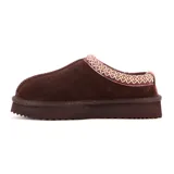 Pantufla tipo mule de cuero gamuzado color marrón, con interior de peluche y detalle de costura decorativa trenzada en el borde superior. Cuenta con una suela de plataforma dentada de goma.