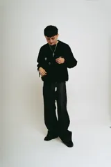 Pantalón de jean negro, corte baggy, confeccionado en denim crudo. Presenta un estampado serigrafiado en blanco con un diseño estilizado en ambos bolsillos traseros y un parche con logo en la cintura.