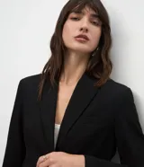 Blazer de corte sastre color negro, con cuello de solapas, cierre frontal de dos botones y forro interno. Presenta una estructura recta y refinada.