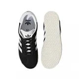 Championes Adidas modelo Gazelle, color negro con las icónicas tres tiras y talón en blanco. Presentan el nombre del modelo en letras doradas en el lateral y una suela de goma texturizada en color crema.