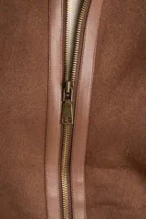 Chaqueta tipo gamulán de calce oversize en color marrón, con cuello y ribetes de corderito en contraste. Presenta cierre frontal de cremallera, bolsillos laterales y detalles de tiras decorativas en material sintético.