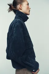 Cazadora estilo bomber confeccionada en piel, con cuello solapa, manga larga y cierre frontal con cremallera oculta y botones a presión. Presenta bolsillos delanteros de plastrón con solapa y botón a presión.