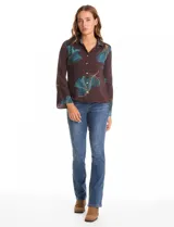 Camisa de crepe con estampado floral en tonos verdes y marrones, cuello con solapa, cierre frontal con botones y detalle de mostacillas bordadas en los hombros. Presenta mangas largas con terminación amplia.