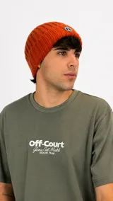 Gorro tipo beanie de punto acanalado en color naranja, con parche circular con logo en la parte frontal.