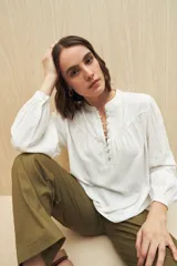 Camisa blanca de viscosa con cuello mao, botonadura parcial, mangas largas abullonadas con puños abotonados y frunces en los hombros.