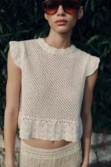 Top de cuello redondo y mangas sisa con volantes, confeccionado en tejido de punto calado con algodón y bajo con detalle de volantes.