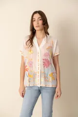 Camisa blanca de seda con bordados florales multicolor, cuello camisero y mangas cortas.