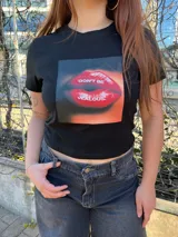 Remera negra corta con estampado frontal de labios rojos y la frase "Don't be jealous.", manga corta y cuello redondo.