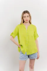 Camisa de lino color verde lima, de calce relajado, con cuello mao, botones al frente y bolsillo en el pecho. Las mangas son cortas y pueden usarse arremangadas.