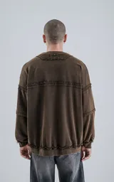 Buzo de cuello redondo color marrón oscuro con efecto desgastado (lavado óxido). Presenta costuras expuestas y detalles de pespunte ondulado en puños y ruedo. Tiene un calce oversize y crop.