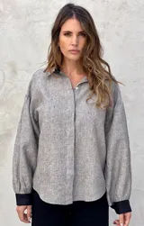 Camisa a rayas verticales grises y blancas, de lino, con cuello clásico, cierre frontal con botones, mangas abullonadas 3/4 con puños elásticos negros y corte holgado.